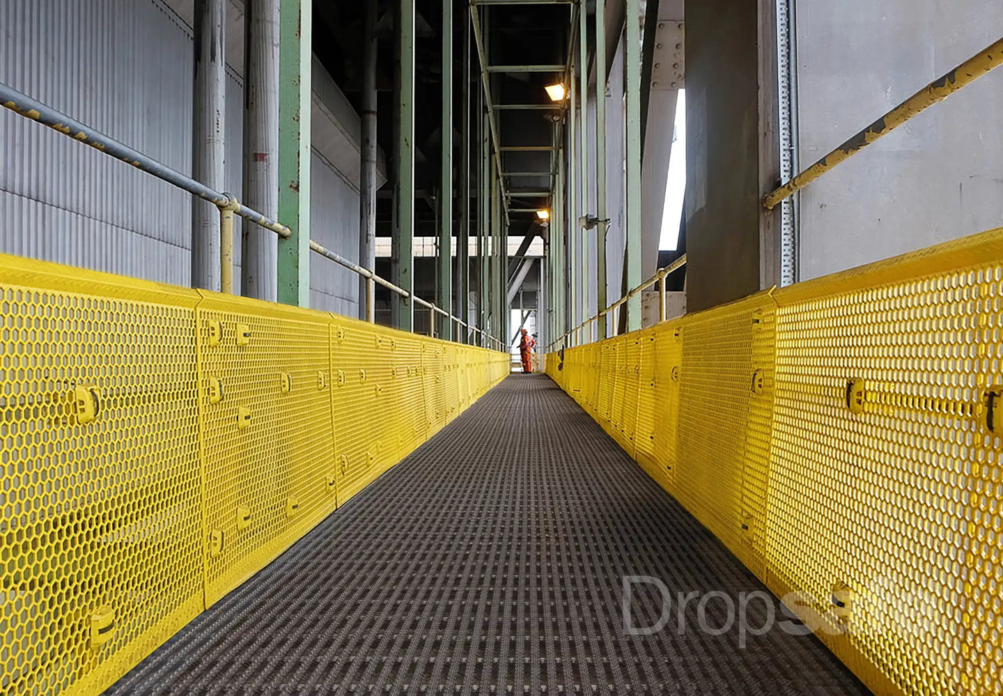 Bright yellow perforated metal safety guardrails line a walkway.
