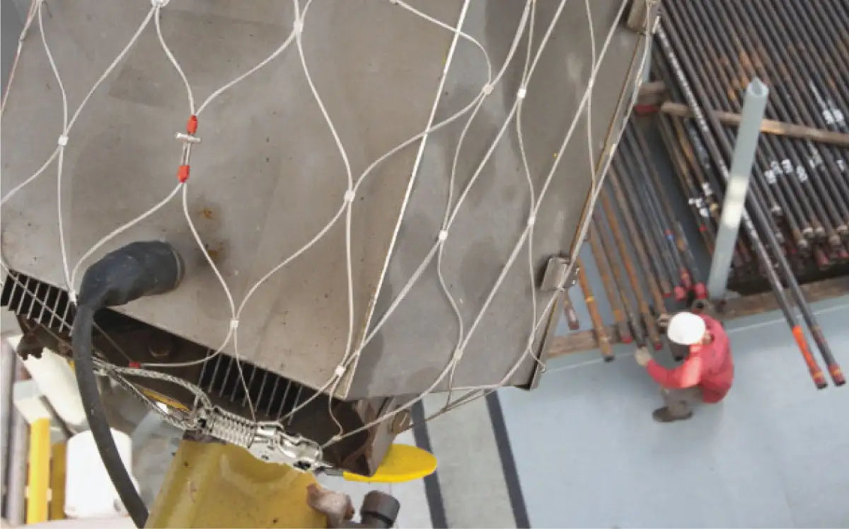 A heavy-duty metallic industrial component with a white netting secured over its surface, featuring red-tipped fasteners and connected to thick black cables.