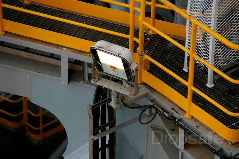 Industrial-grade white floodlight mounted on a yellow safety railing.