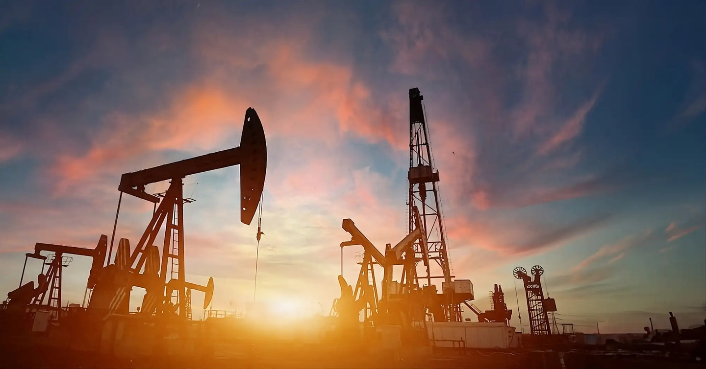 Silhouetted oil pumps stand against a vibrant sunset sky.