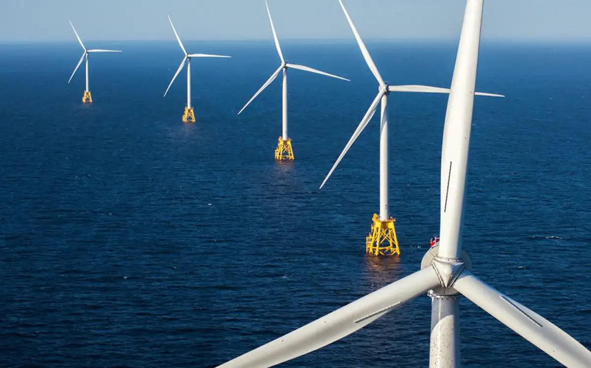 White offshore wind turbines with yellow base structures standing in the deep blue ocean.
