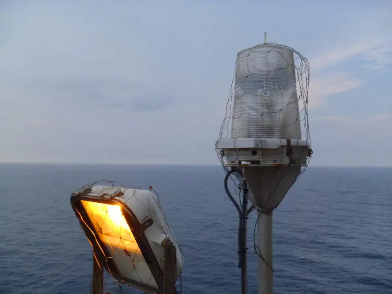 White, weathered lighthouse lantern with a wire mesh cage and glass housing.