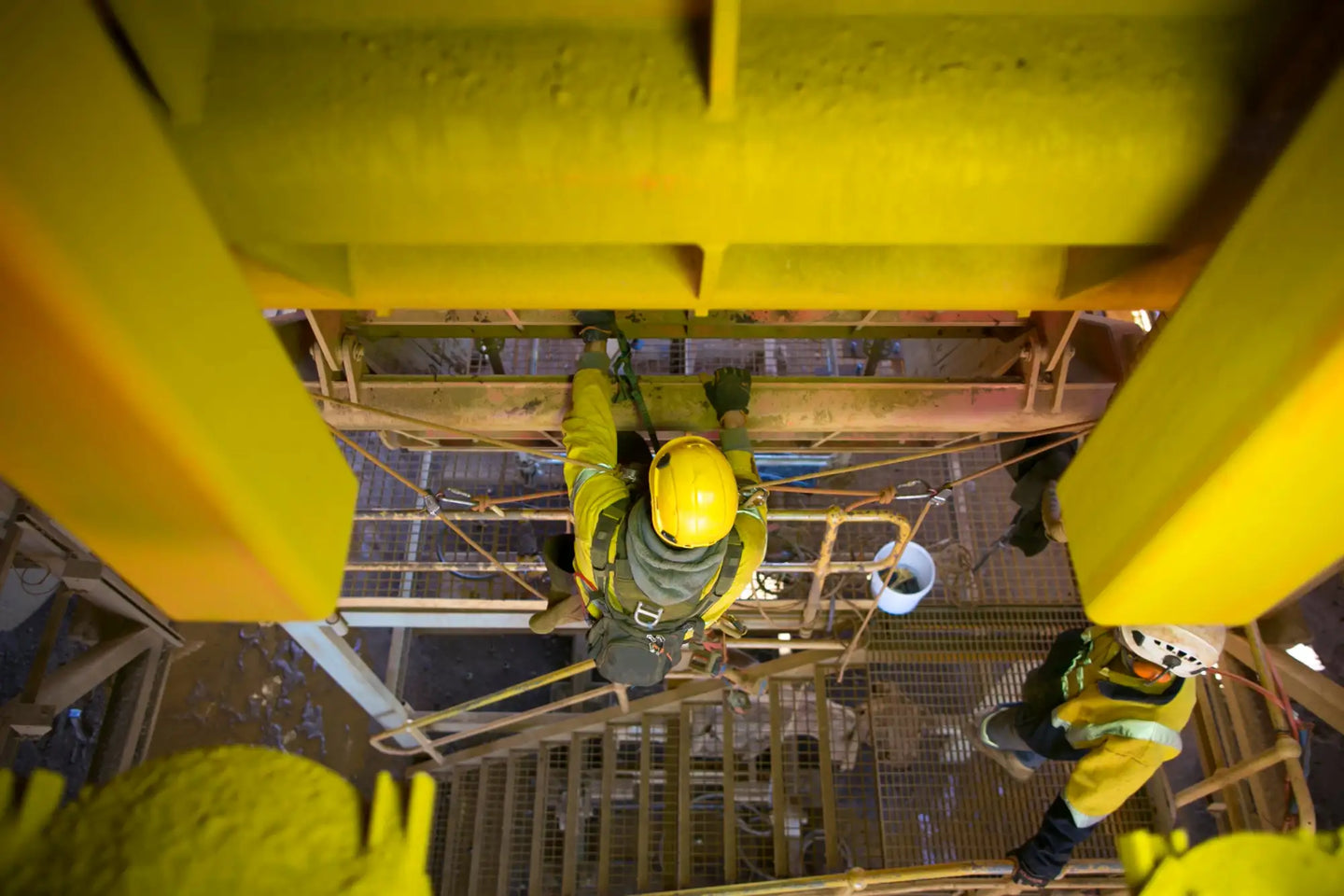 Worker in yellow safety gear and helmet suspended on scaffolding.