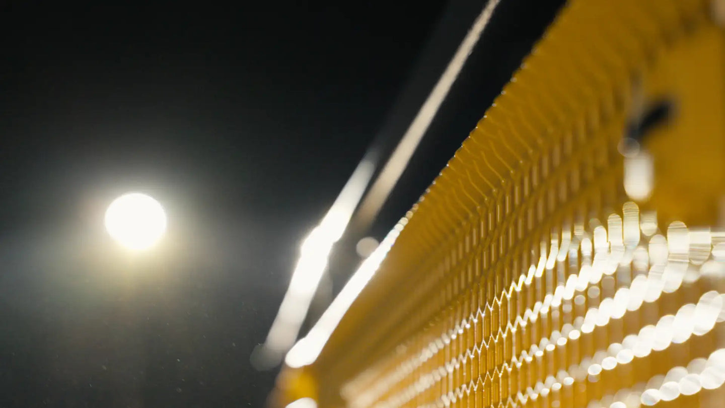 Yellow metal tennis net with a wavy, textured surface and bright white light reflections