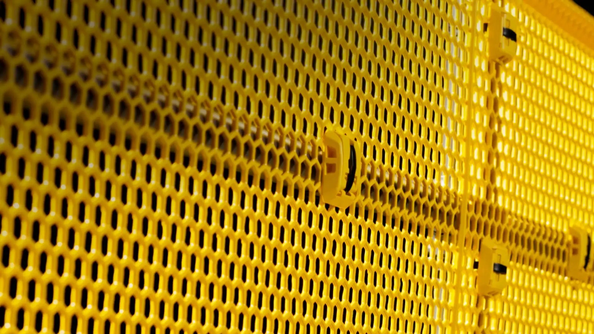 Yellow plastic mesh panel with a repeating hexagonal pattern and small black fasteners along the edges